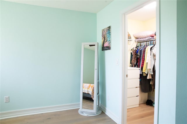 unfurnished bedroom with a walk in closet, baseboards, a closet, and light wood-style flooring