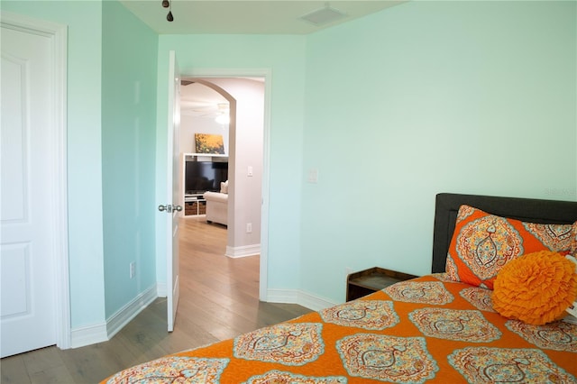 bedroom featuring visible vents, arched walkways, baseboards, and wood finished floors