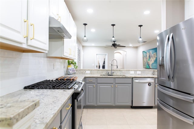 kitchen with gray cabinets, under cabinet range hood, a sink, appliances with stainless steel finishes, and decorative backsplash