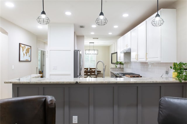 kitchen with under cabinet range hood, decorative backsplash, light stone counters, and freestanding refrigerator