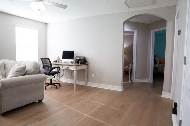 office space featuring baseboards, arched walkways, light wood-style floors, and a ceiling fan