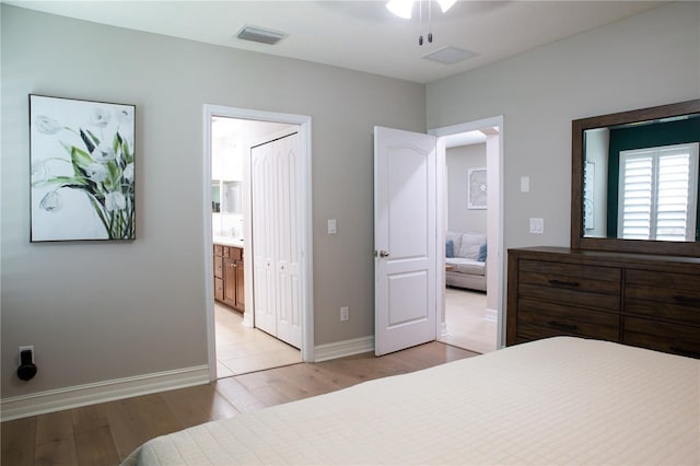 bedroom with baseboards, visible vents, ensuite bath, and light wood-style floors