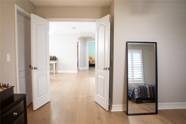 corridor featuring baseboards, arched walkways, and light wood-style floors