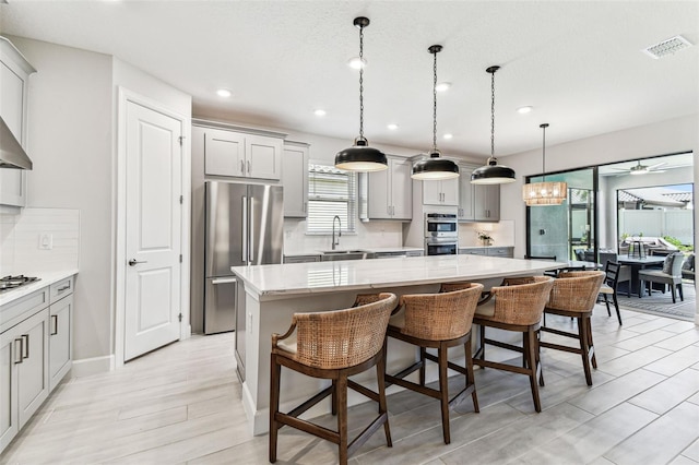 kitchen with visible vents, gray cabinetry, a sink, a kitchen island, and appliances with stainless steel finishes