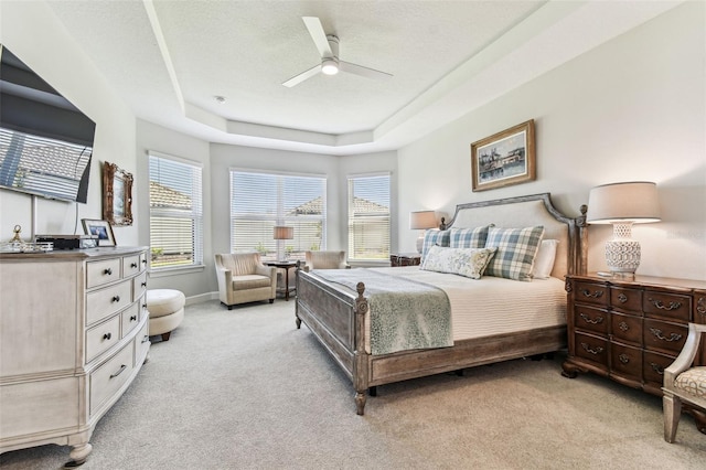 bedroom featuring a tray ceiling, light carpet, multiple windows, and a textured ceiling