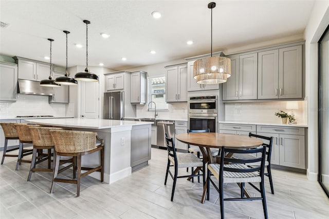 kitchen featuring a kitchen island, gray cabinets, stainless steel appliances, under cabinet range hood, and a kitchen breakfast bar