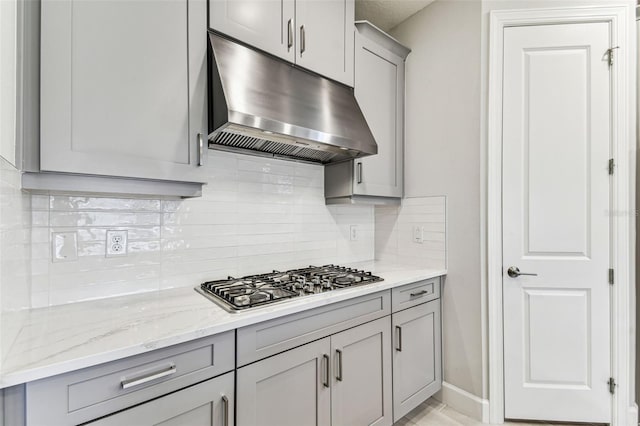 kitchen featuring tasteful backsplash, gray cabinetry, light stone countertops, under cabinet range hood, and stainless steel gas stovetop