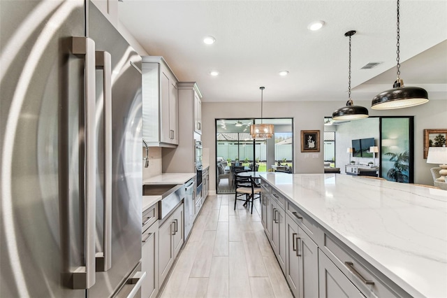 kitchen featuring light stone countertops, visible vents, gray cabinets, freestanding refrigerator, and pendant lighting