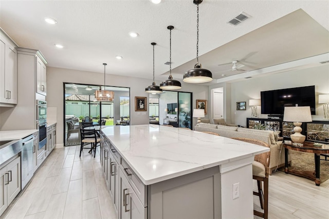 kitchen with visible vents, gray cabinetry, a kitchen island, stainless steel double oven, and hanging light fixtures