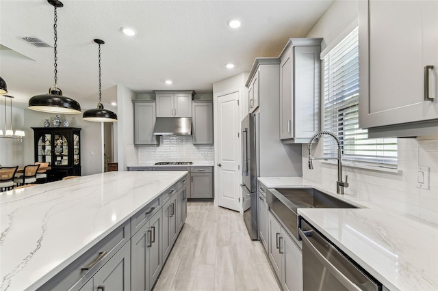 kitchen featuring visible vents, under cabinet range hood, gray cabinets, stainless steel appliances, and a sink