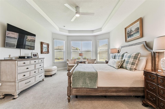 bedroom featuring light carpet, a tray ceiling, a textured ceiling, baseboards, and ceiling fan