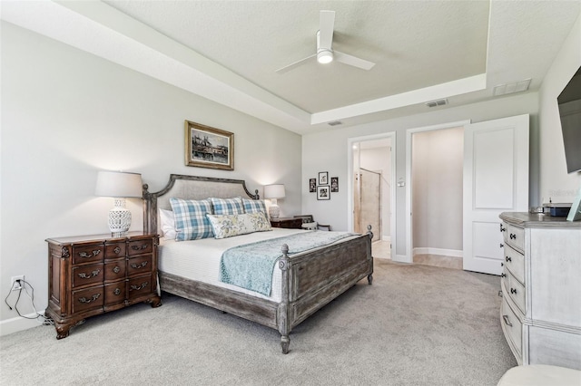 bedroom featuring a raised ceiling, light colored carpet, visible vents, and baseboards