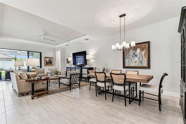 dining space with baseboards, a raised ceiling, and ceiling fan with notable chandelier