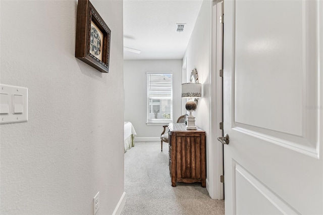 hall with baseboards, visible vents, and light carpet