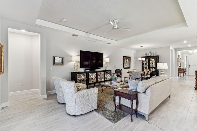 living room with a tray ceiling, baseboards, visible vents, and ceiling fan with notable chandelier