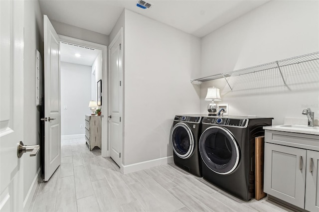 clothes washing area featuring baseboards, visible vents, cabinet space, a sink, and washer and clothes dryer