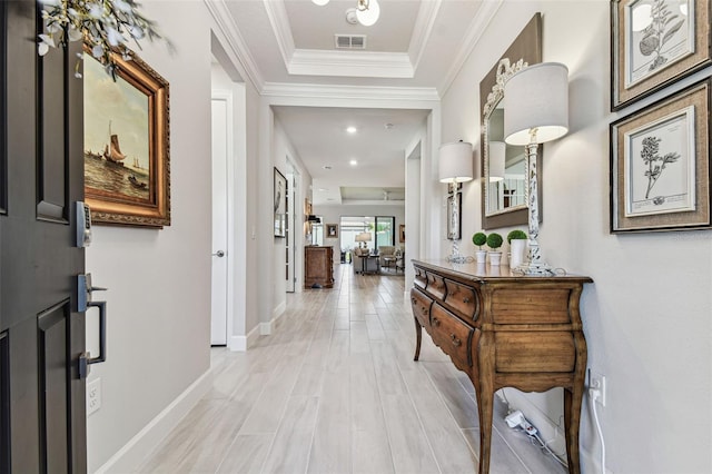 corridor with visible vents, a tray ceiling, light wood-style floors, crown molding, and baseboards