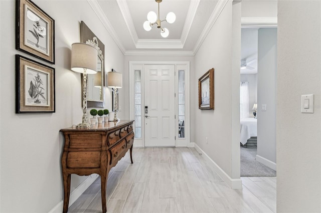 entryway with baseboards, crown molding, light wood-type flooring, a raised ceiling, and a chandelier