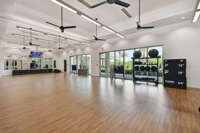 gym with visible vents, a ceiling fan, wood finished floors, a high ceiling, and baseboards