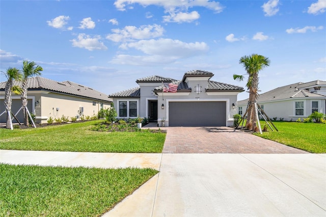 mediterranean / spanish-style house with a tile roof, a front yard, stucco siding, decorative driveway, and an attached garage