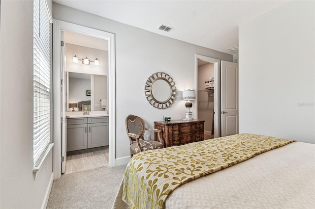 bedroom with visible vents, a walk in closet, light carpet, ensuite bathroom, and a sink