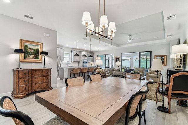 dining space with a tray ceiling, visible vents, light wood-style floors, and ceiling fan with notable chandelier