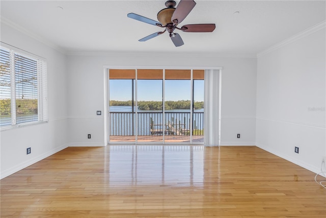 unfurnished room featuring wood finished floors, baseboards, ceiling fan, a water view, and crown molding