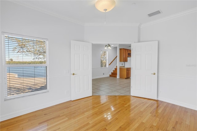 empty room featuring stairs, visible vents, light wood finished floors, and ornamental molding