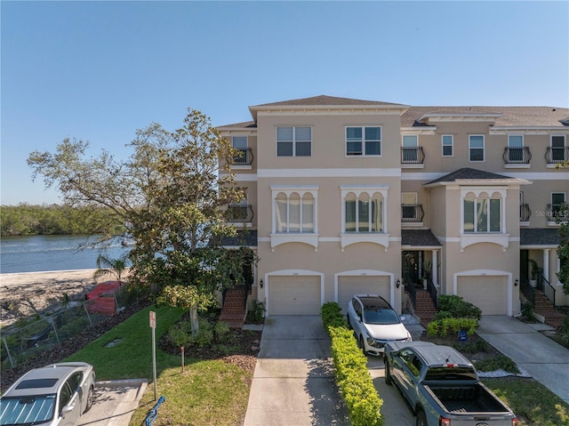 view of front of house with driveway, an attached garage, stucco siding, stairs, and a water view