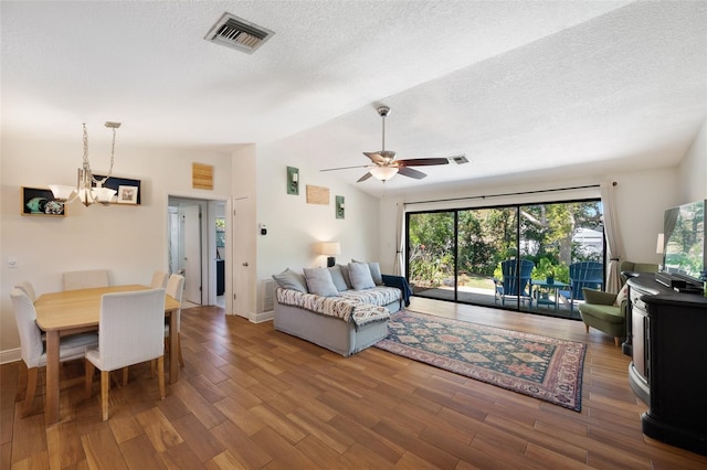 living area with visible vents, ceiling fan with notable chandelier, a textured ceiling, wood finished floors, and vaulted ceiling