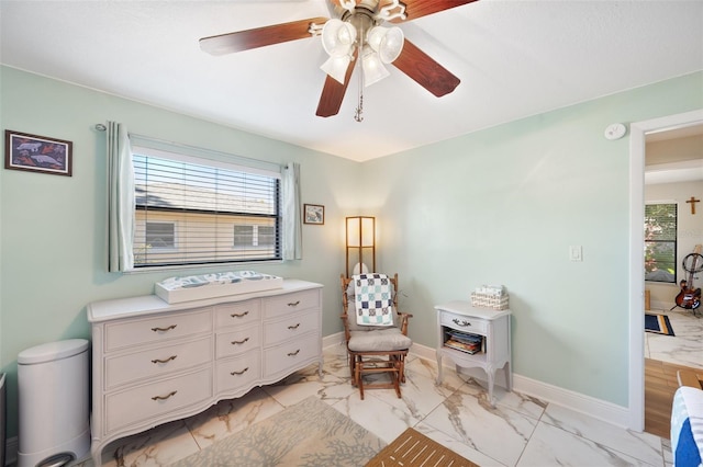 living area featuring baseboards, marble finish floor, and ceiling fan