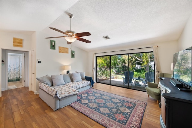 living area with a ceiling fan, visible vents, lofted ceiling, a textured ceiling, and light wood-type flooring