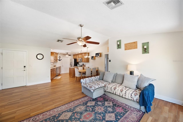 living area with visible vents, light wood-style flooring, lofted ceiling, and a ceiling fan