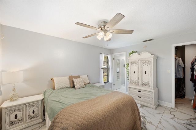 bedroom with visible vents, a walk in closet, marble finish floor, a ceiling fan, and baseboards