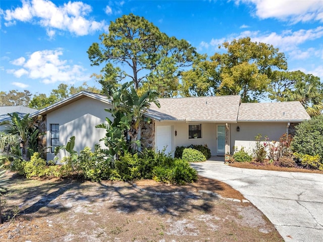 ranch-style home with concrete driveway, a garage, roof with shingles, and stucco siding