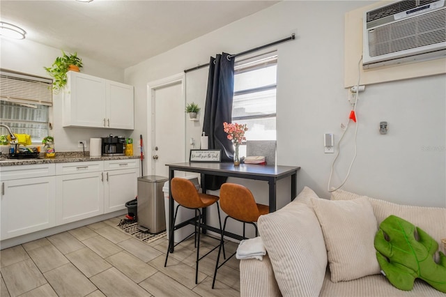 kitchen with white cabinetry, a wall mounted AC, and light stone countertops