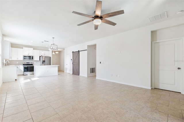 unfurnished living room with a sink, a barn door, visible vents, and ceiling fan