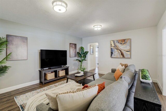 living room with arched walkways, baseboards, and wood finished floors