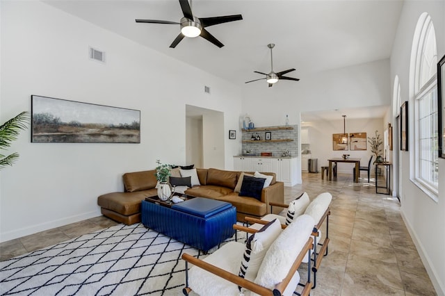 living room with visible vents, baseboards, a towering ceiling, and a ceiling fan