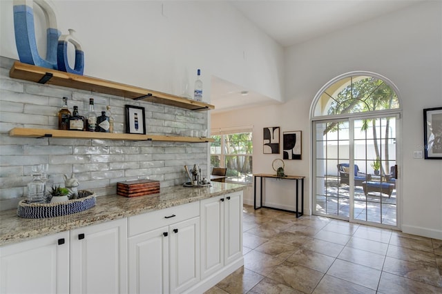 kitchen featuring decorative backsplash, white cabinets, light stone countertops, and open shelves