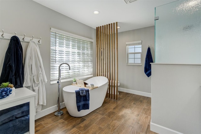 full bath featuring recessed lighting, a freestanding tub, baseboards, and wood finished floors