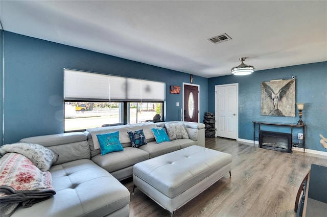 living room featuring visible vents, wood finished floors, baseboards, and a glass covered fireplace