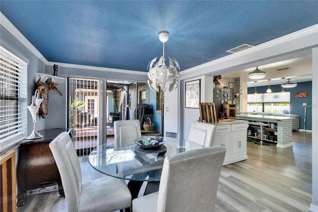 dining area featuring baseboards, visible vents, light wood-style flooring, crown molding, and a notable chandelier