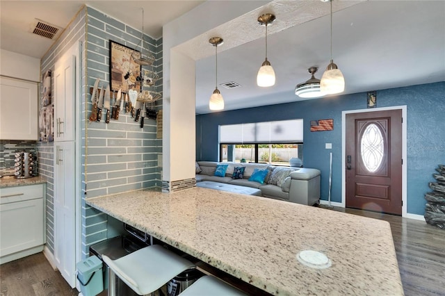 kitchen featuring dark wood-type flooring, tasteful backsplash, a peninsula, and visible vents