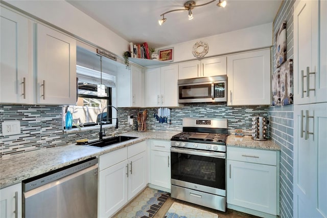 kitchen featuring light stone counters, decorative backsplash, white cabinets, stainless steel appliances, and a sink