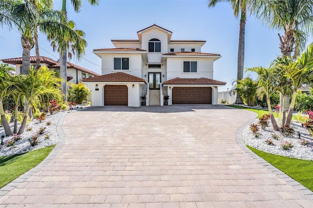 mediterranean / spanish-style house with stucco siding, french doors, a garage, a tile roof, and decorative driveway