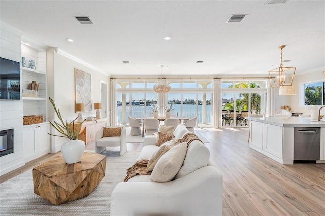 living area with a chandelier, visible vents, light wood-style flooring, and ornamental molding