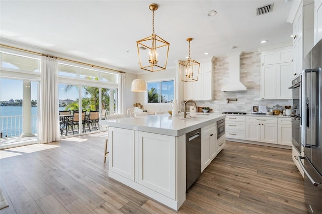 kitchen featuring visible vents, a notable chandelier, a sink, backsplash, and wall chimney exhaust hood