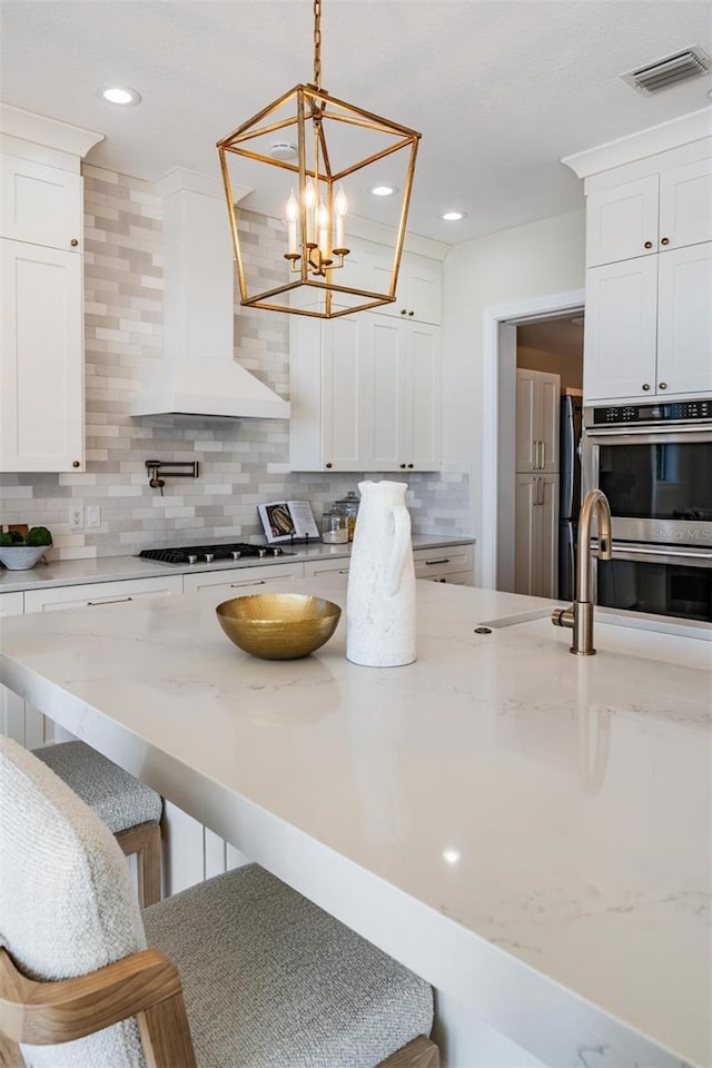 kitchen with visible vents, a breakfast bar, stainless steel appliances, decorative backsplash, and wall chimney exhaust hood