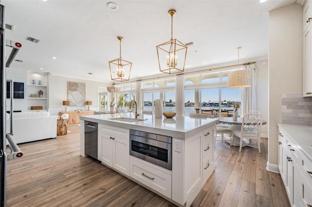 kitchen featuring stainless steel microwave, a healthy amount of sunlight, light countertops, light wood-style flooring, and a sink